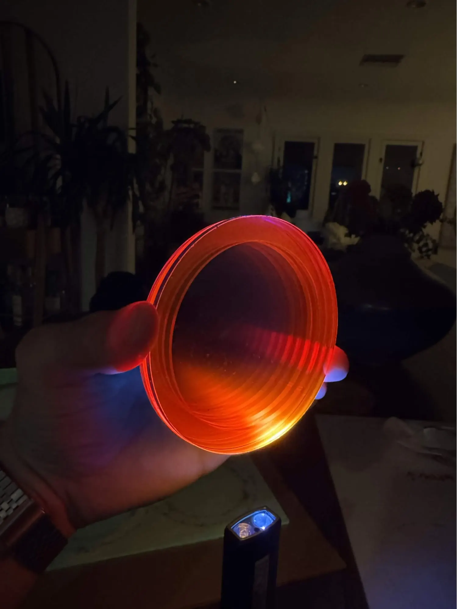 A fluorescent acrylic ring glowing orange in a hand, lit from the edge by a blacklight