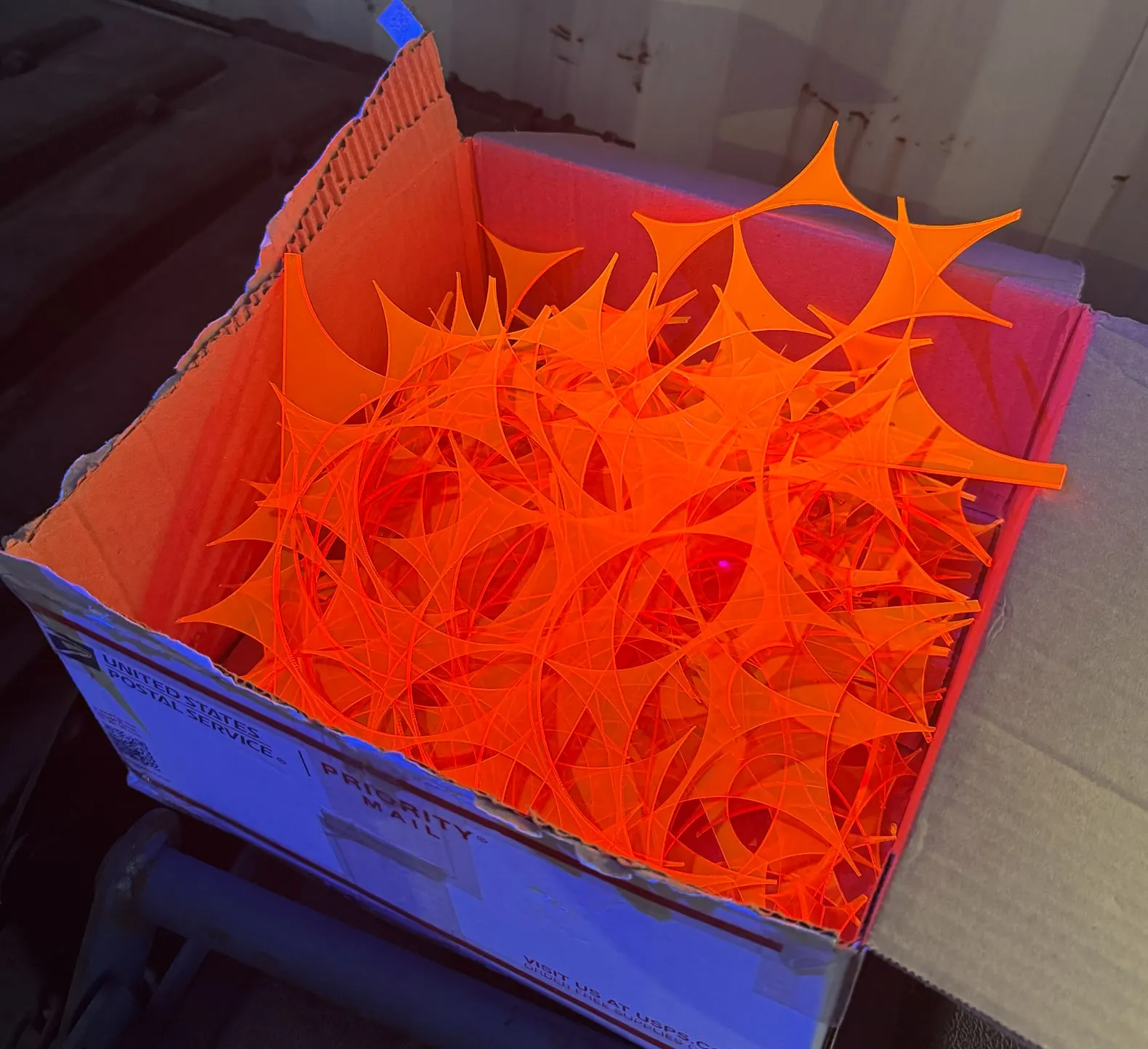 A cardboard box full of glowing orange acrylic offcuts