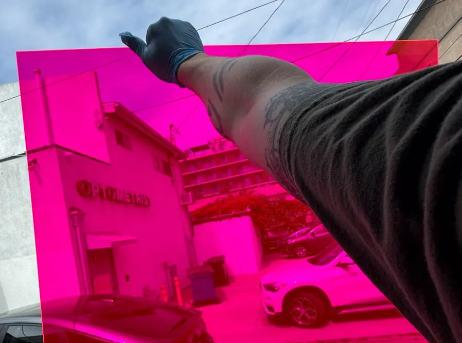 An arm holding a sheet of fluorescent pink acrylic up against the sky