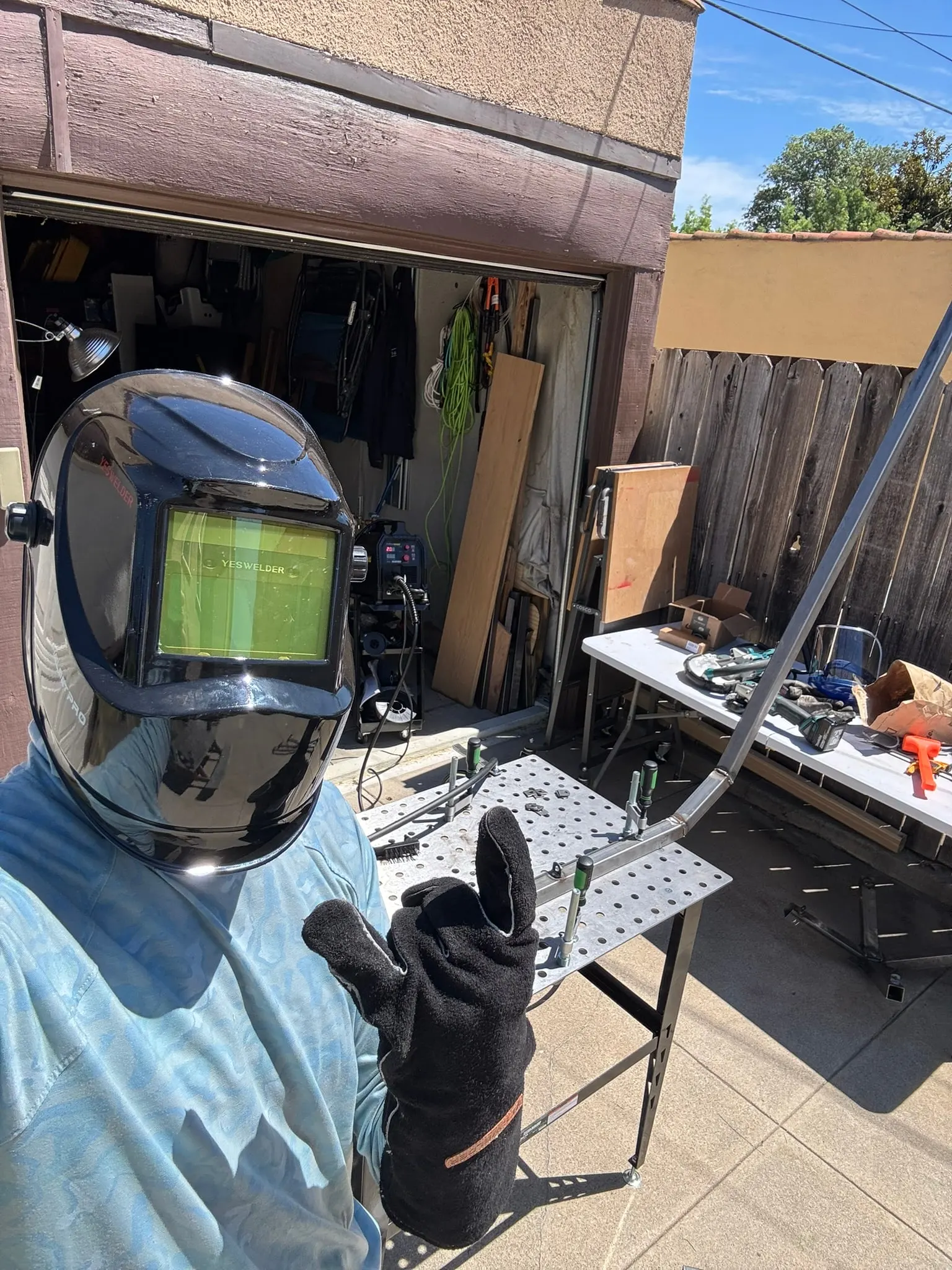 Julien in a welding helmet and jacket in the backyard