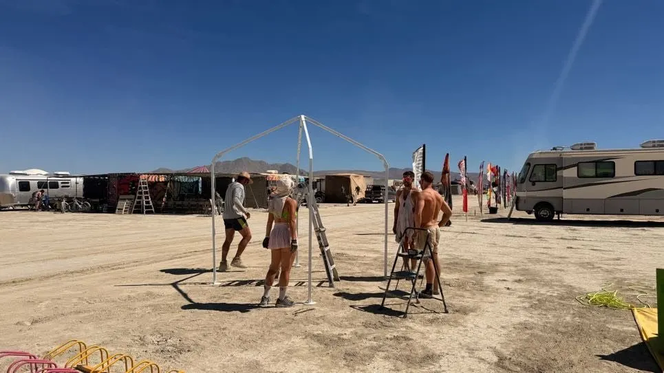 Two people raising the frame on the playa beside RVs