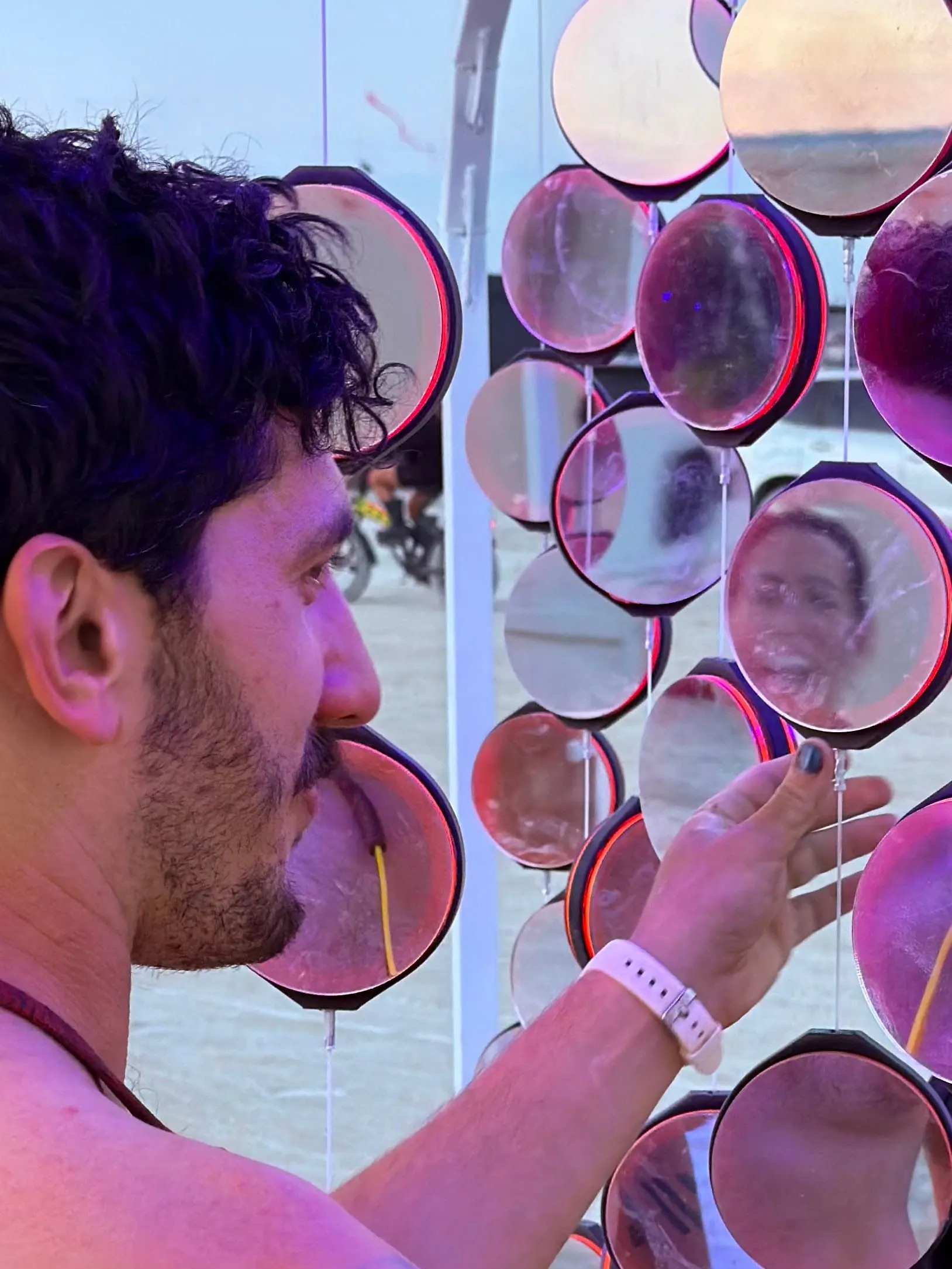 Julien leaning into the hanging mirrors in daylight