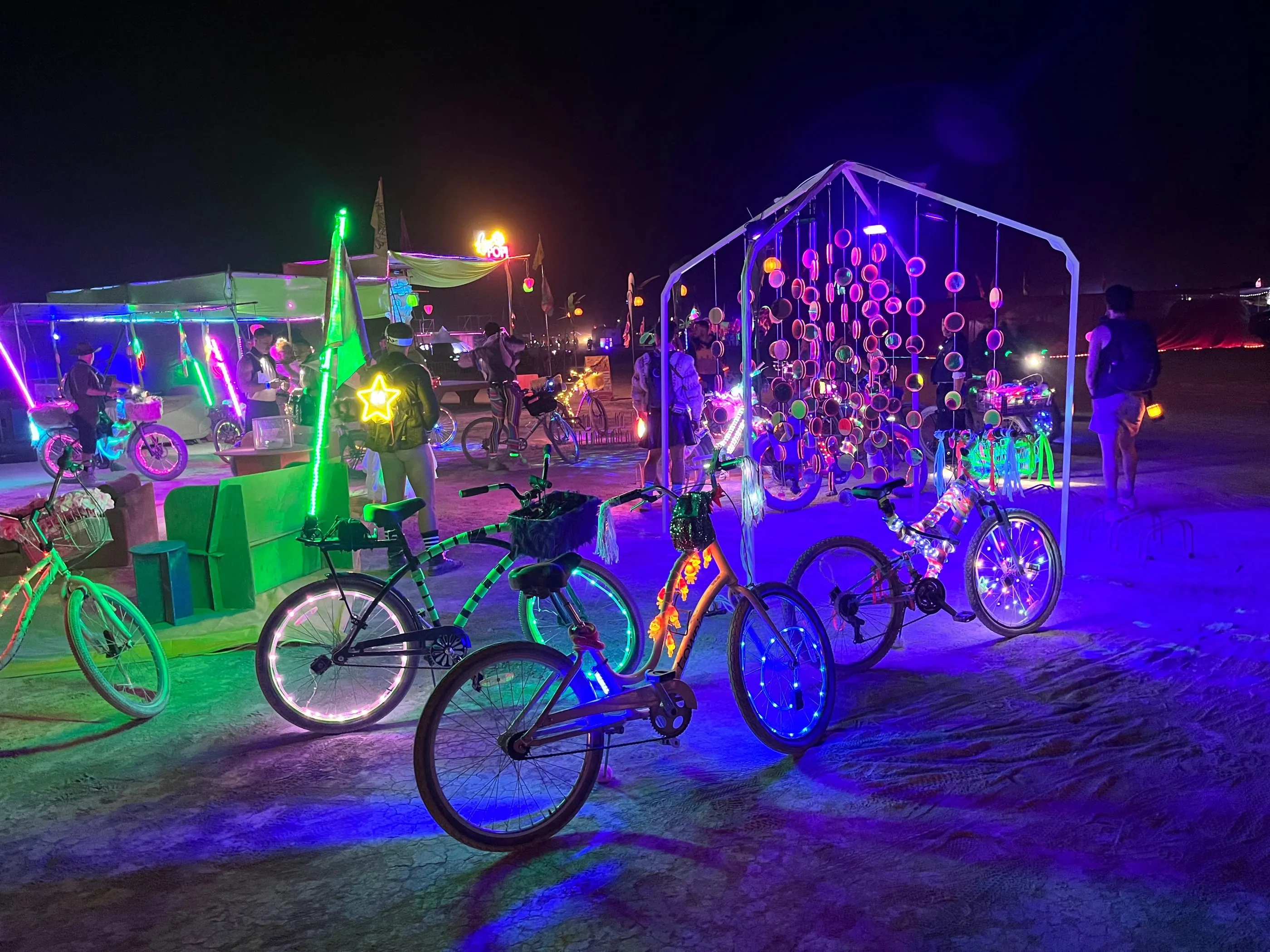The installation at night, glowing pink and violet under UV, with lit-up bikes parked in front