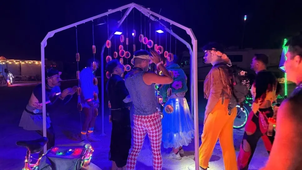 A crowd in costume gathered around the glowing installation at night