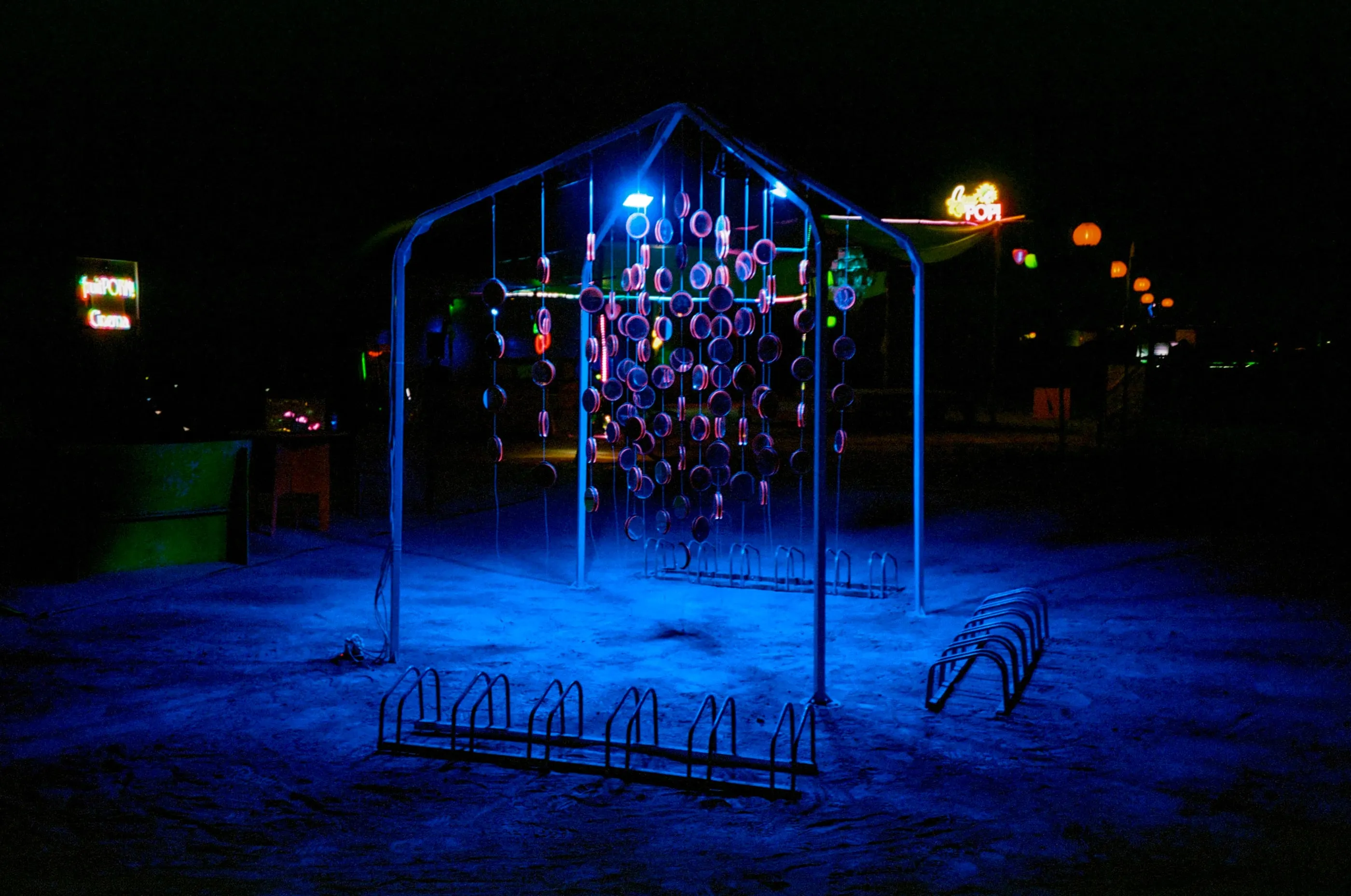 Film photo of the installation at night, its frame and mirrors glowing blue and violet on the playa
