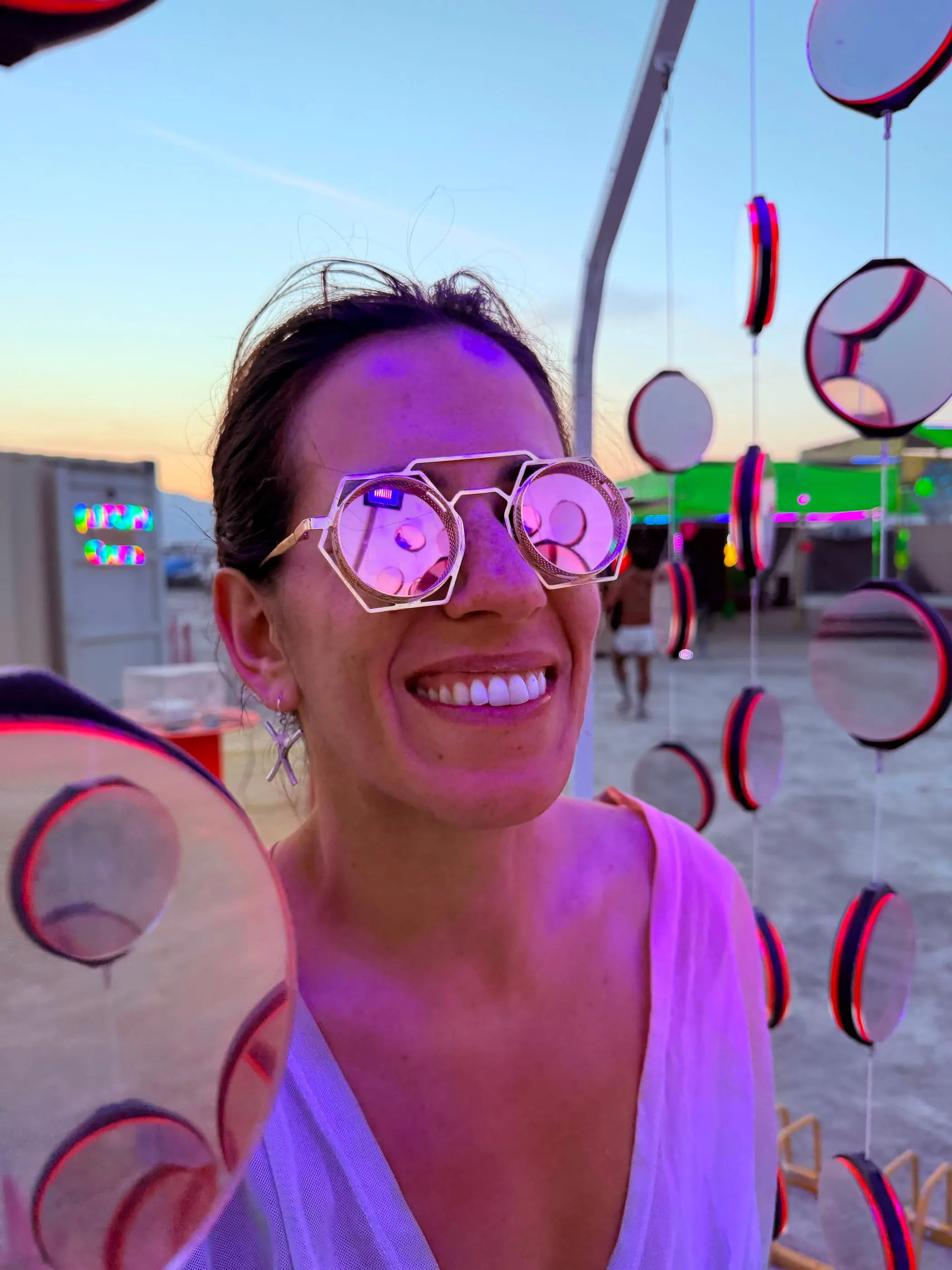 A smiling visitor in heart-shaped glasses beside the mirrors at sunset